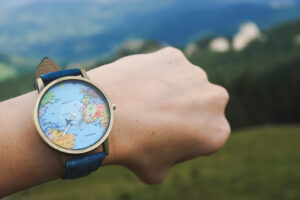 Hand mit Armbanduhr, im Ziffernblatt Weltkarte und Flugzeuge.